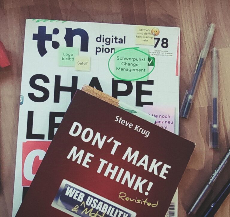 Eine Zeitschrift und ein Buch liegen auf einem Holztisch. Die Zeitschrift liegt unten. Es ist das t2n Magazin Nummer 78 mit dem Titel Shape, Lead, Change, Repeat. Darauf liegt das Buch "Don't make me think!" von Steve Krug. Um die Zeitschrift und das Buch liegen verschiedene Stifte und ein Spitzer in Form eines gelben Bleistifts.